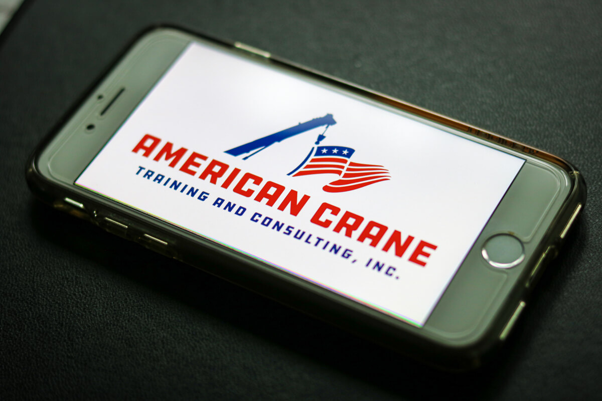 Photo of a phone showing the logo for a crane training and consulting company called American Crane Training & Consulting